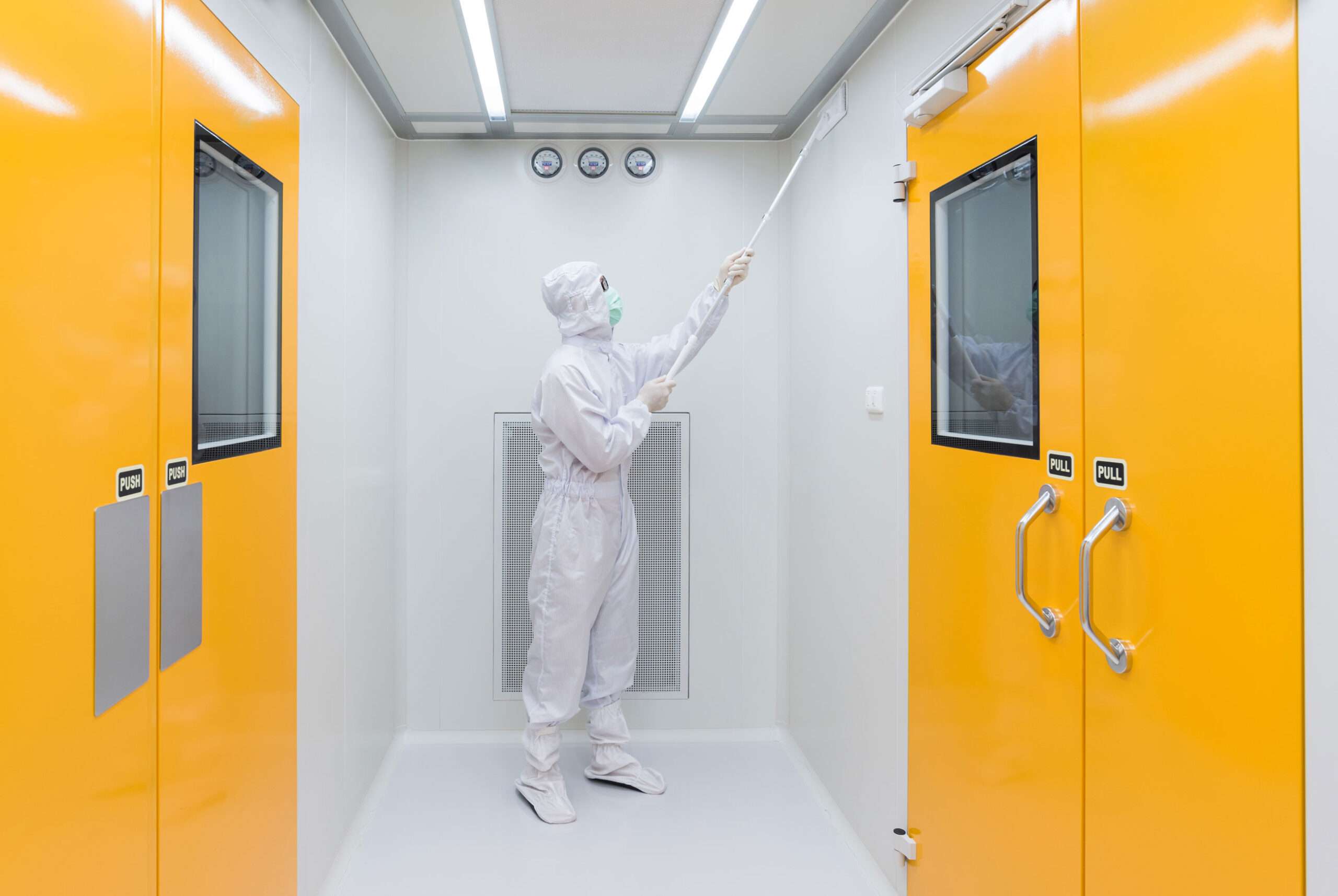 Fully PPE-covered Pii scientist cleaning a sterile hallway outside tightly sealed labs to prevent cross-contamination of HPAPIs.