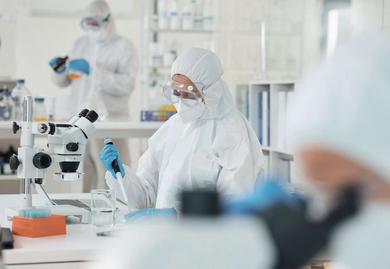 Fully PPE-covered Pii scientists working on HPAPIs in a sterile lab environment.